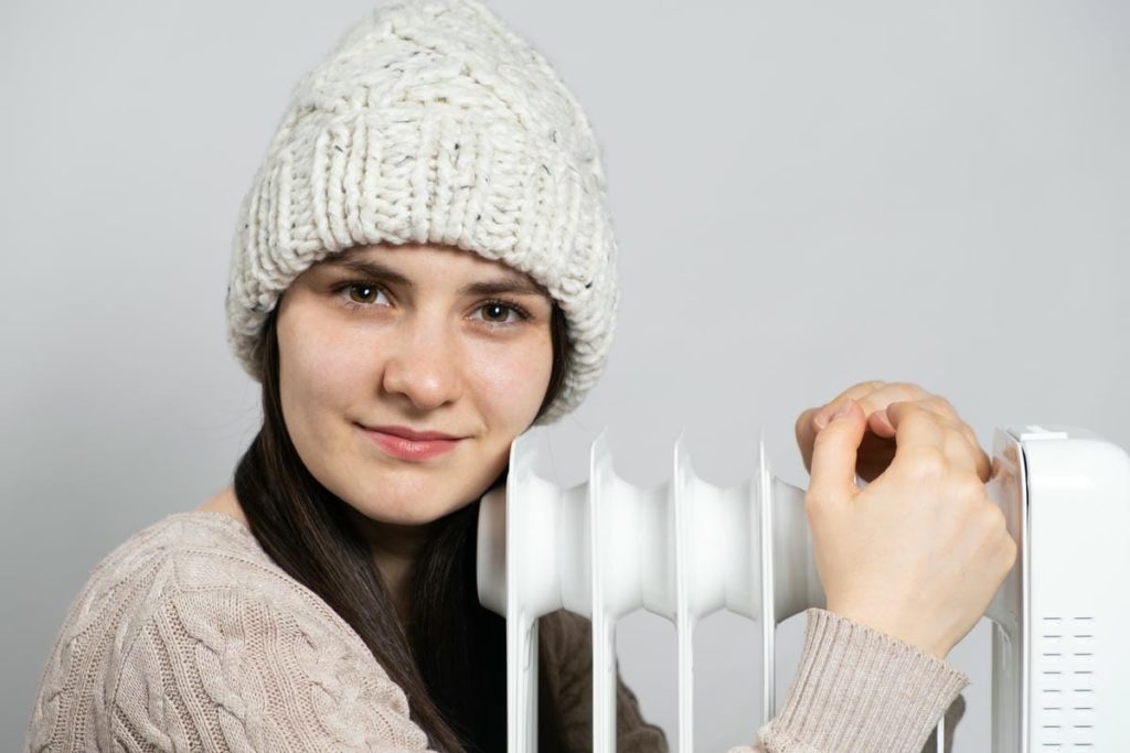 femme brune avec bonnet serrant radiateur a huile se rechauffe hiver