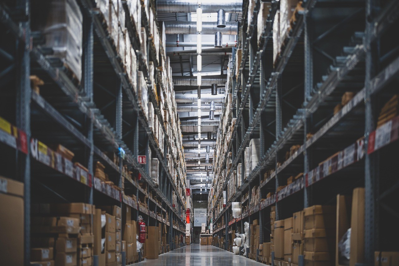 Arnaque au prix du climatiseur pendant la canicule : comment ne pas payer trop cher 4 Allée d'entrepôt avec des rayonnages chargés de cartons, illustrant la tension sur les stocks