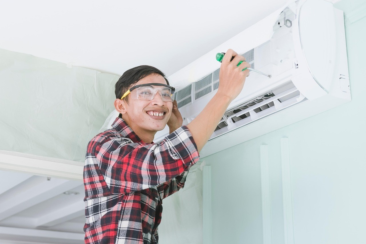 Technicien souriant fixant une unité intérieure de climatisation murale