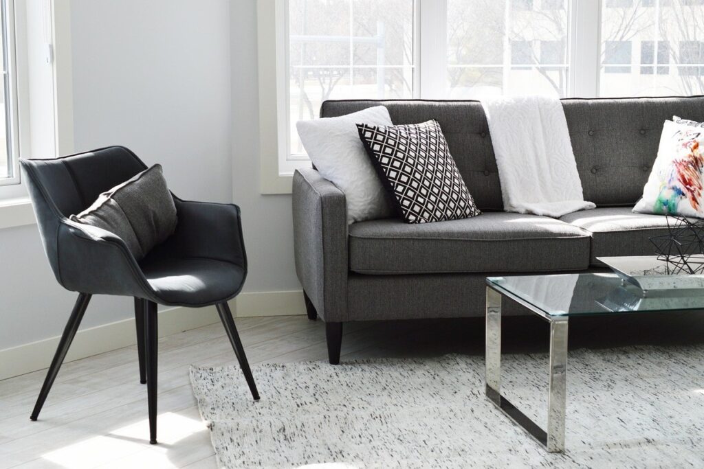 Salon lumineux avec canapé gris, fauteuil noir et table basse en verre