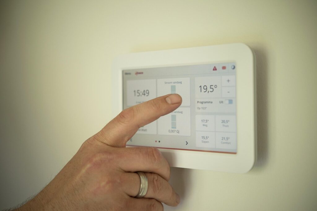 Main réglant un thermostat connecté mural affichant température et heure