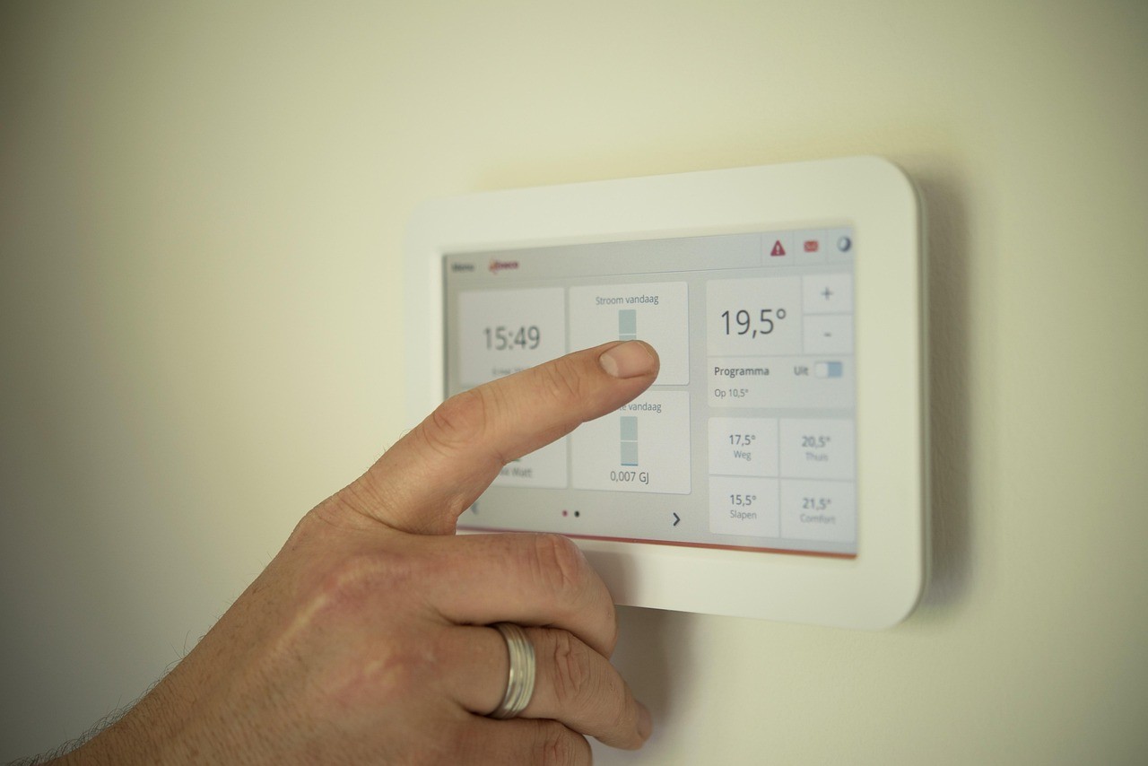 Main réglant un thermostat connecté mural affichant température et heure