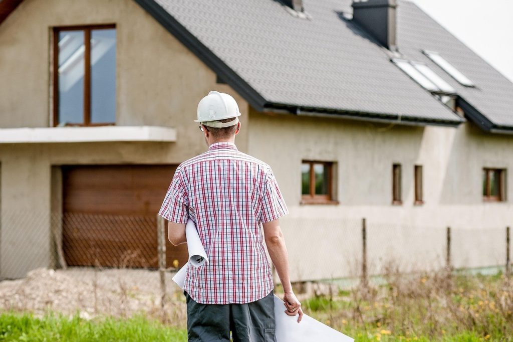 Professionnel du bâtiment, plans sous le bras, devant un pavillon en cours de travaux